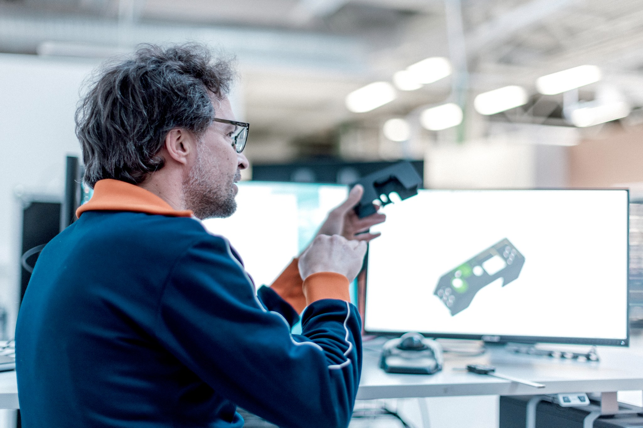 A man holding a 3D-printed object in his hand in front of a computer screen with the same object on it